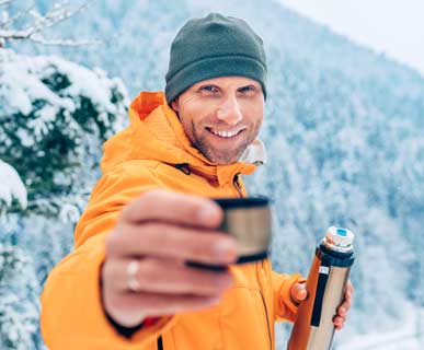 Smiling man in orange jacket offering hot drink