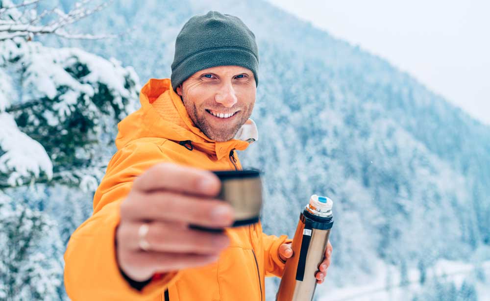 Smiling man in orange jacket pouring hot drink